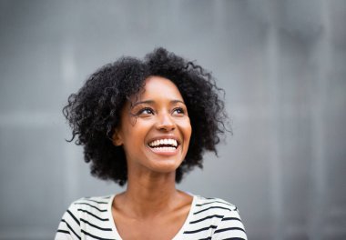 Gri duvarda gülümseyen ve yukarı bakan güzel Afro-Amerikan kadın.