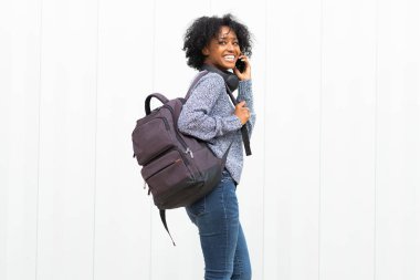Beyaz duvarda cep telefonuyla yürüyen ve konuşan genç Afro-Amerikan kadın portresi