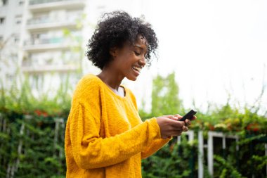 Açık havada cep telefonuna bakan mutlu genç zenci kadın.