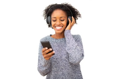 Cep telefonu ve kulaklıklı gülümseyen siyah bir kadın izole edilmiş beyaz arka planda müzik dinliyor.