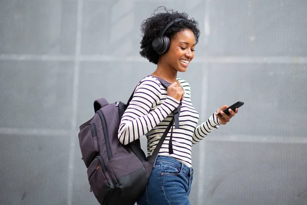 サイドポートレート幸せな若い黒の女性旅行者は 携帯電話やヘッドフォンで音楽を聴くと離れて見て — ストック写真