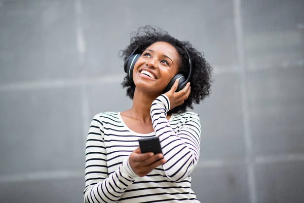 携帯電話やヘッドフォンで音楽を聞いて離れて見て肖像幸せな若い黒人女性 — ストック写真