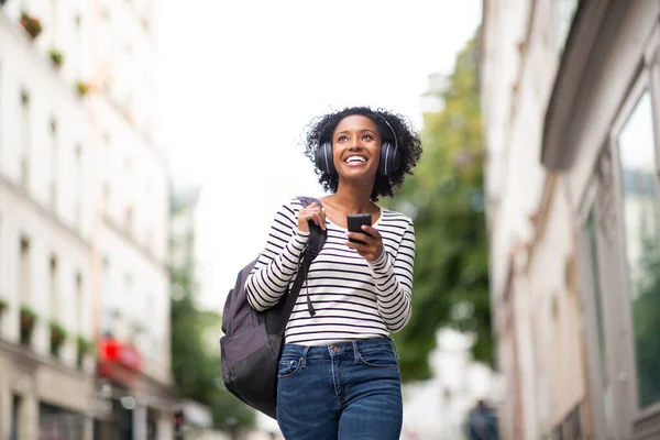 Portret Uśmiechnięta Młoda Afroamerykanka Chodząca Telefonem Komórkowym Słuchająca Muzyki Słuchawkami — Zdjęcie stockowe