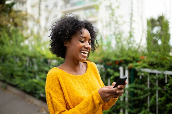 Portrait happy young black woman looking at mobile phone outdoors