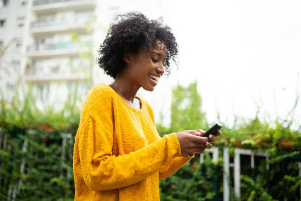 サイドポートレート幸せな若いです黒女性見ます携帯電話屋外 — ストック写真