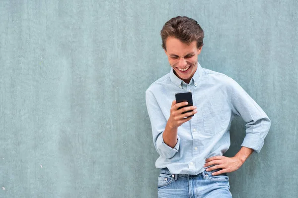 Portret Gelukkige Jongeman Leunend Tegen Muur Kijkend Naar Mobiele Telefoon — Stockfoto