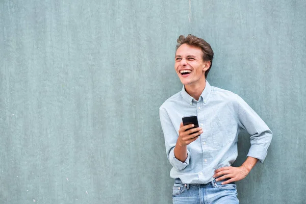 Портрет Счастливого Молодого Человека Прислонившегося Стене Держащего Мобильный Телефон Отворачивающегося — стоковое фото