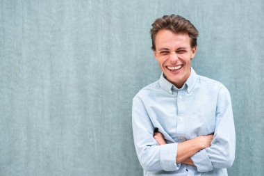 Kollarını kavuşturup duvara yaslanan gülen genç adam portresi.