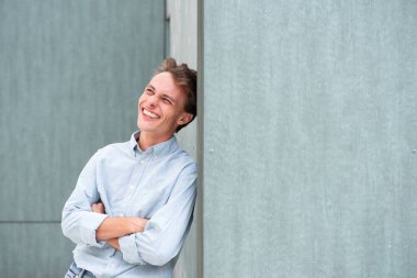 Duvara yaslanmış, kollarını kavuşturmuş, başka tarafa bakıp gülen yakışıklı bir genç portresi.