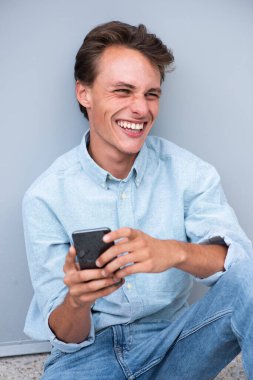 Portre mutlu genç adam oturuyor ve cep telefonuna bakıyor.
