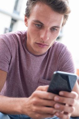 Yakın plan yakışıklı genç adam cep telefonuna bakıyor.