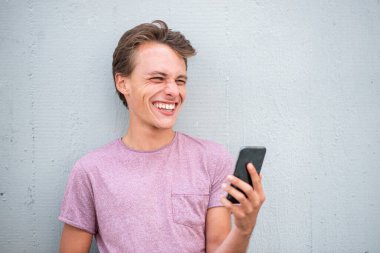 Cep telefonuyla duvara yaslanmış gülen genç adam portresini yakından çek.