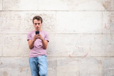 Dışarda duvara yaslanmış ve cep telefonuna bakan genç bir portre.