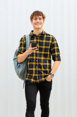 Beyaz arka planda cep telefonu ve çantası olan mutlu genç adam portresi.