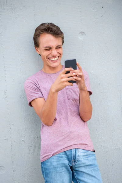 Portret Lachende Jongeman Leunend Tegen Muur Kijkend Naar Mobiele Telefoon — Stockfoto