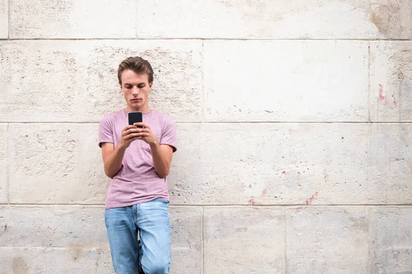 Portret Jongeman Leunend Tegen Muur Buiten Kijkend Naar Mobiele Telefoon — Stockfoto