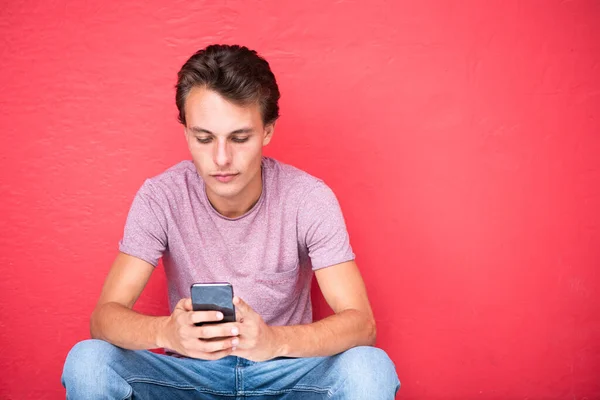 Close Portret Jongeman Zitten Door Rode Muur Zoek Naar Mobiele — Stockfoto