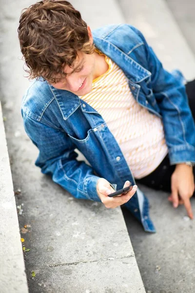Портрет Сверху Счастливого Молодого Человека Сидящего Снаружи Ступеньках Смотрящего Мобильный — стоковое фото