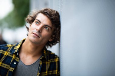 Portre çekici genç adam gri duvara yaslanmış, başka tarafa bakıyor. 