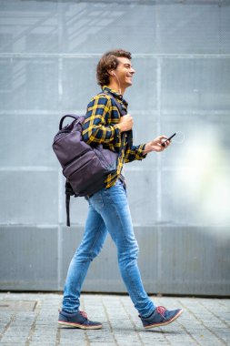 Tam vücut portresi mutlu gezgin cep telefonu ve kulaklıkla yürüyor.