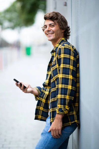 Портрет Улыбающийся Молодой Человек Прислонившийся Стене Держа Руках Мобильный Телефон — стоковое фото