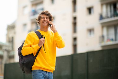 Cep telefonuyla yürüyen ve konuşan mutlu erkek öğrenci portresi