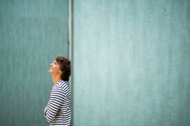 Yeşil duvara yaslanmış gülümseyen yakışıklı genç adam yukarı bakıyor.