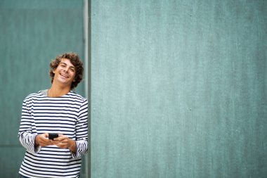 Yeşil arka planda cep telefonuyla gülen yakışıklı genç adam portresi.