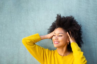 Güzel, Afro saçlı, mavi arka planda gülümseyen Afro-Amerikan kadın portresi.