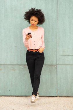 Tam boy portre güzel Afrikalı Amerikalı kadın yeşil duvarda cep telefonuyla yürüyor