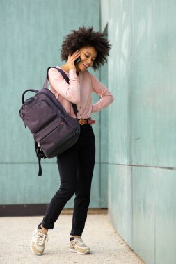 Tam vücut portresi. Genç Afrikalı Amerikalı kadın cep telefonuyla konuşuyor. 