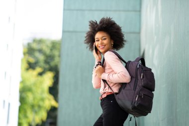 Yan portre mutlu genç Afrikalı Amerikalı kadın çantalı cep telefonuyla konuşuyor.