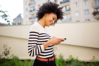 Dışarıda cep telefonuyla yürüyen gülümseyen genç zenci kadın.