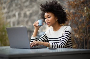 Laptop ve kahveyle oturan genç kadının portresi.