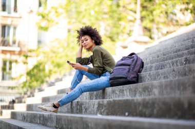 Cep telefonu ve kulaklıkla merdivenlerde oturan güzel bir genç kadın.