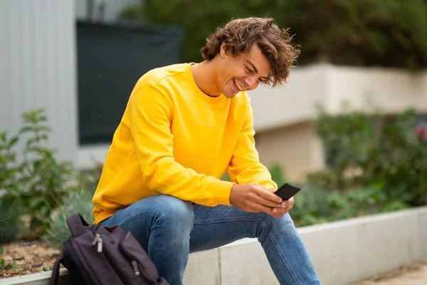 Портрет Смеющегося Юноши Сидящего Снаружи Смотрящего Мобильный Телефон — стоковое фото