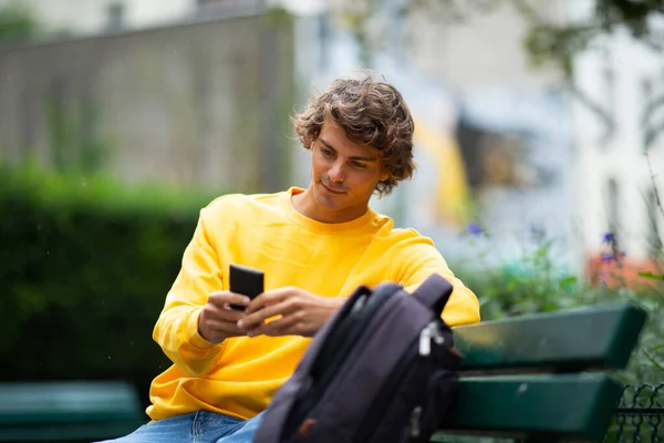 Portret Młodego Człowieka Siedzącego Ławce Parku Patrzącego Telefon Komórkowy — Zdjęcie stockowe
