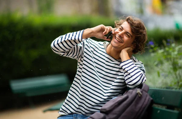 Портрет Красивый Молодой Улыбающийся Мужчина Сидящий Скамейке Парке Разговаривающий Телефоном — стоковое фото