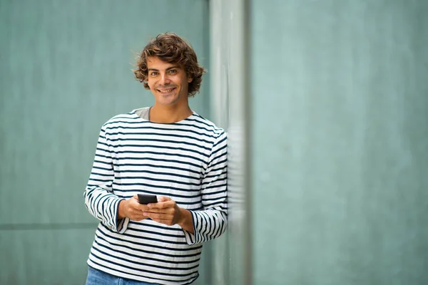 Portrait smiling young man leaning against green wall holding cellphone
