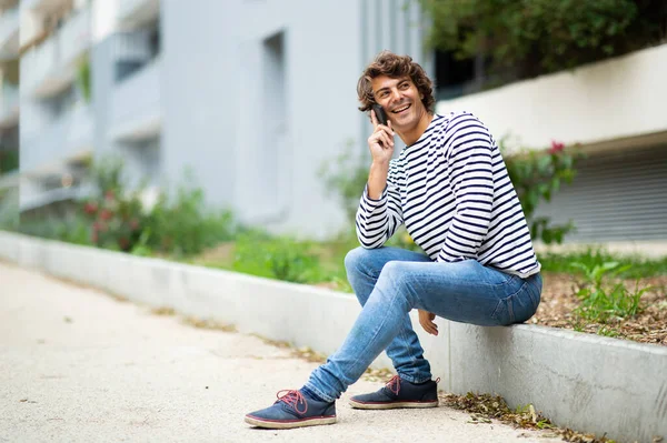 サイドポートレート笑顔ハンサムな若いです男座っています外で街の話とともに携帯電話 — ストック写真