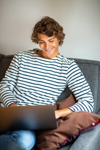 Portrait smiling young man sitting on couch at home with laptop