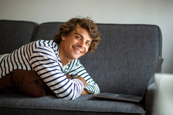 Portret Jonge Lachende Man Liggend Bank Thuis Met Laptop Computer — Stockfoto