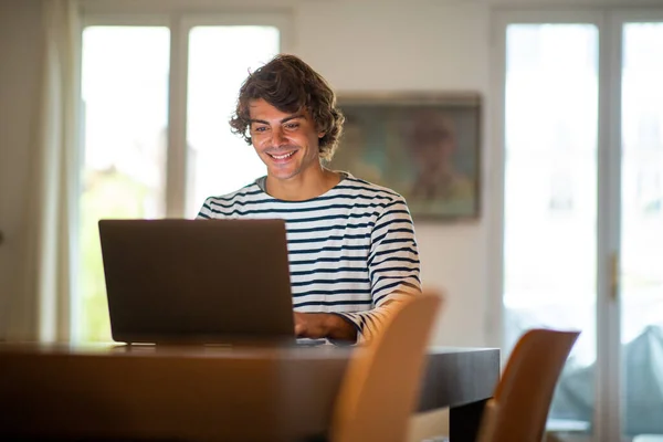 Portrait smiling young man sitting at home working with laptop computer