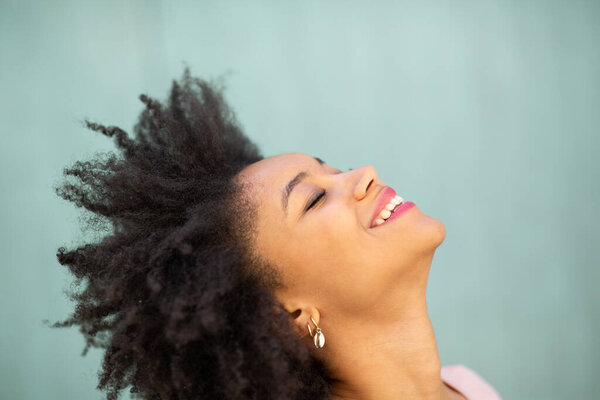 Close up side portrait beautiful young black woman with afro hair laughing against green background 