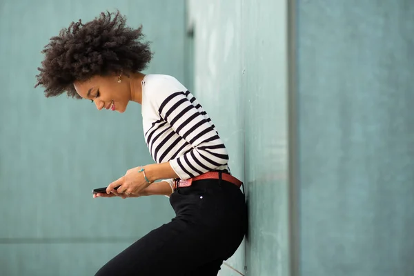 年轻而快乐的非洲裔美国女人靠在墙上 拿着手机 — 图库照片