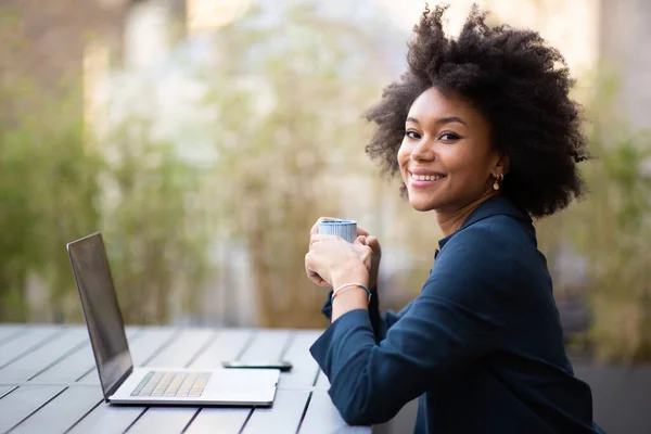 サイドポートレート笑顔若いアフリカ系アメリカ人ビジネス女性で座っているラップトップとコーヒーのカップ — ストック写真