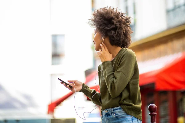 サイドポートレート若い黒の女性が音楽を聴くとイヤホンや市内のスマートフォン — ストック写真