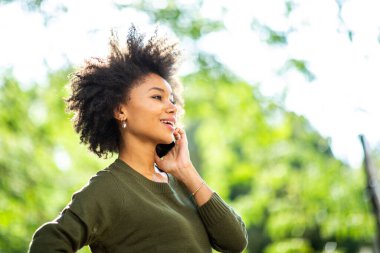 Yan portreyi kapat mutlu siyah kadın dışarıda cep telefonuyla konuşuyor.