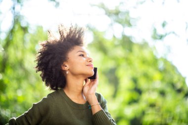Yan portreyi kapat. Genç siyah kadın dışarıda cep telefonuyla konuşuyor.