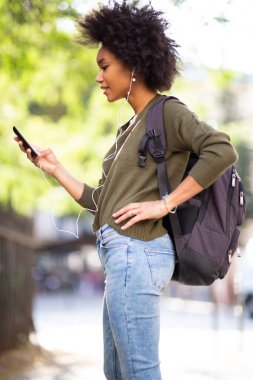 Kentte cep telefonu ve kulaklıkları olan Afro-Amerikan bir kadının yan portresi.